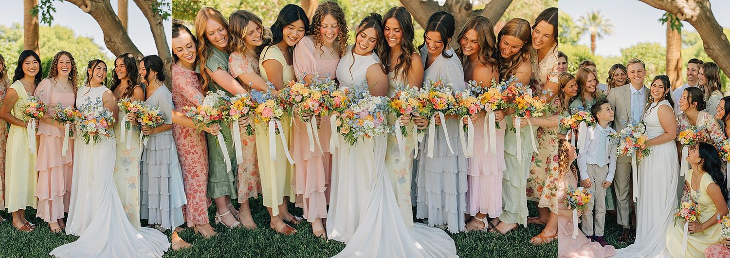 A bride in white surrounded by bridesmaids in pastel dresses holding colorful bouquets at an outdoor wedding.