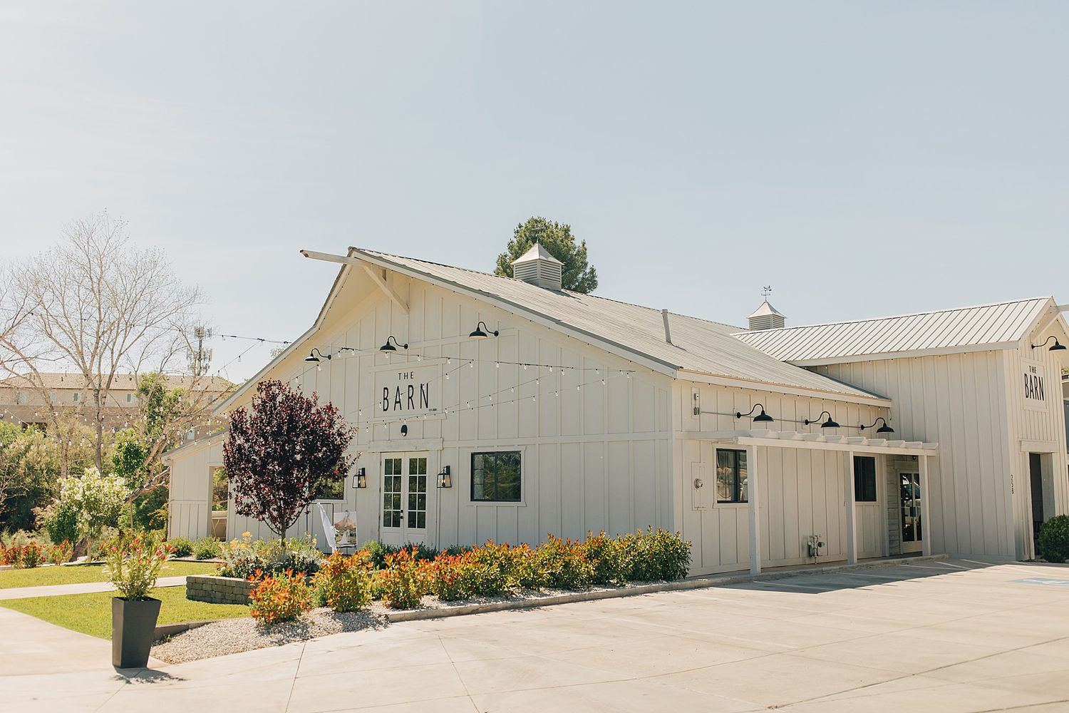 Charming white barn wedding venue exterior with manicured landscaping and colorful flowers on a sunny day.