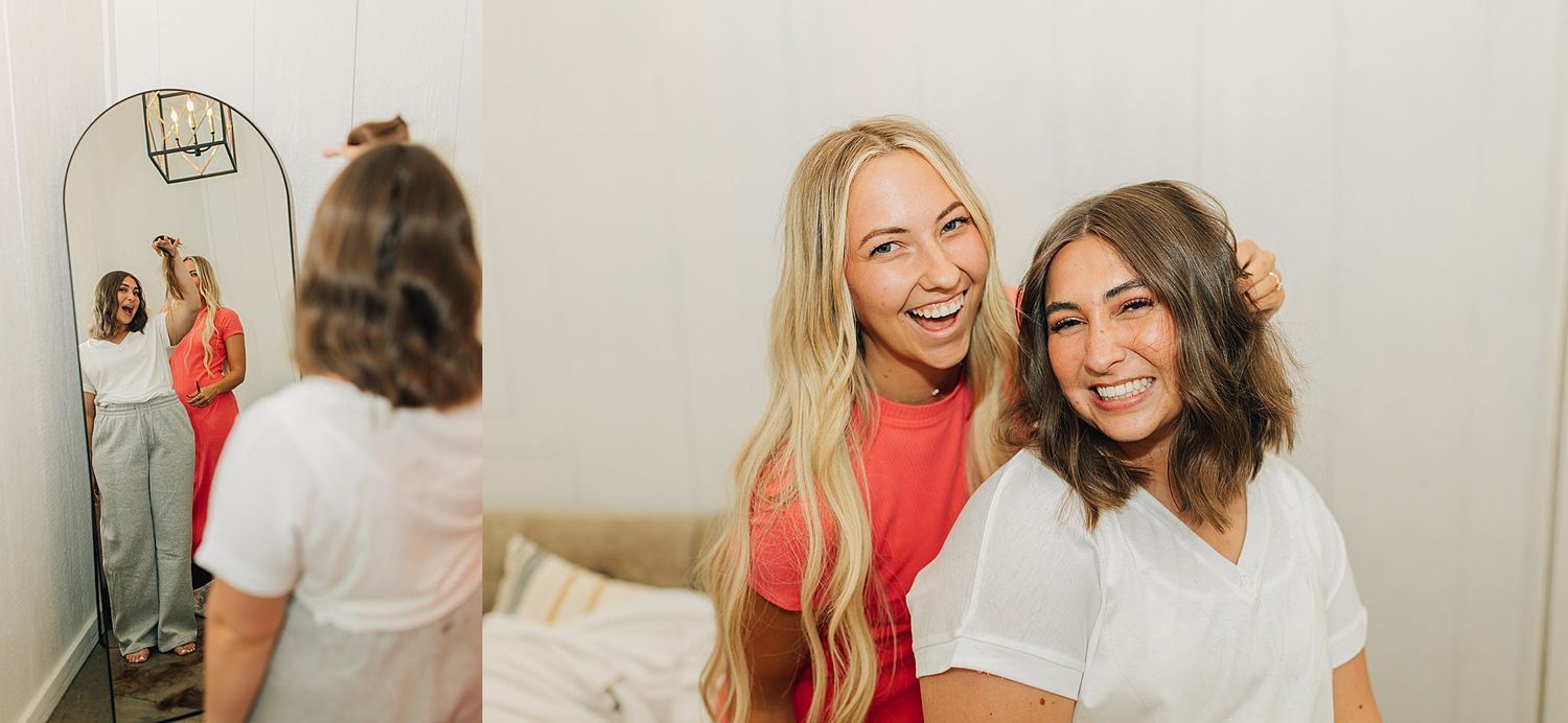 Two smiling women pose together in a bright bedroom, with their reflection visible in a mirror behind them.