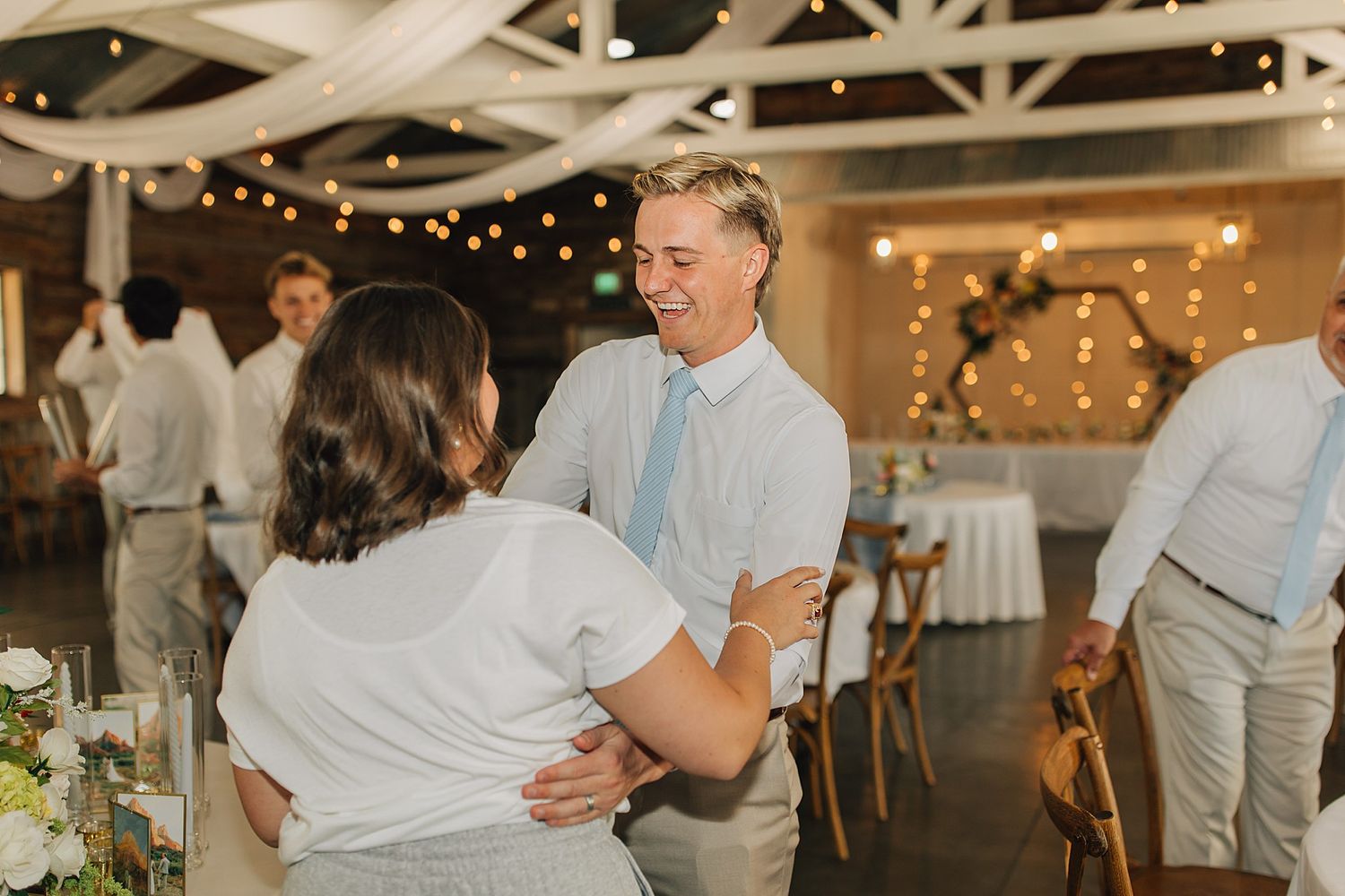 Couple dancing and smiling at a wedding reception with string lights and floral decorations in background.