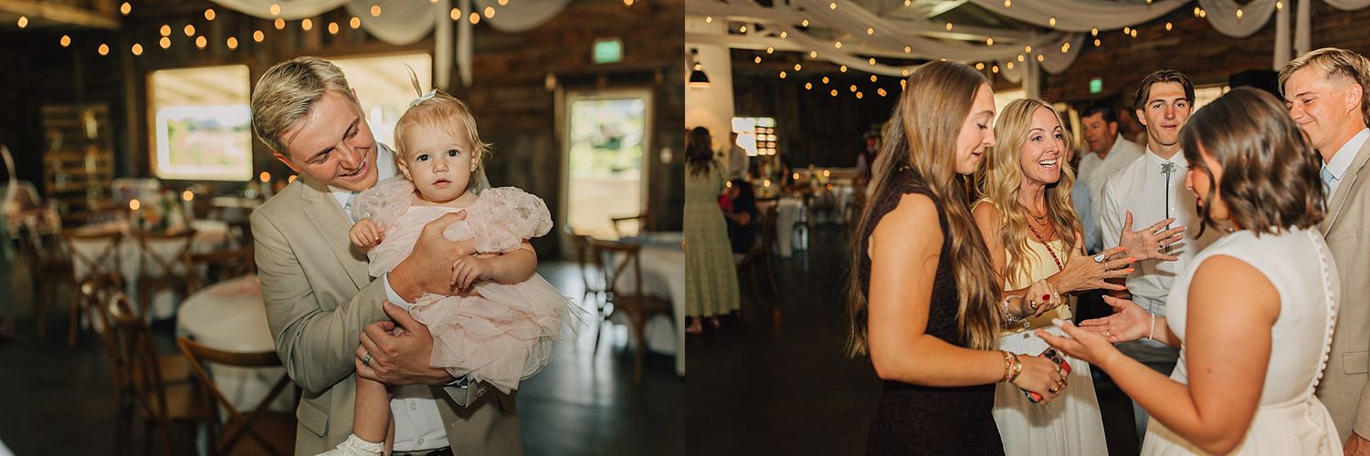 A grandfather holds a baby at a rustic wedding reception while guests celebrate and dance in the warmly lit venue.