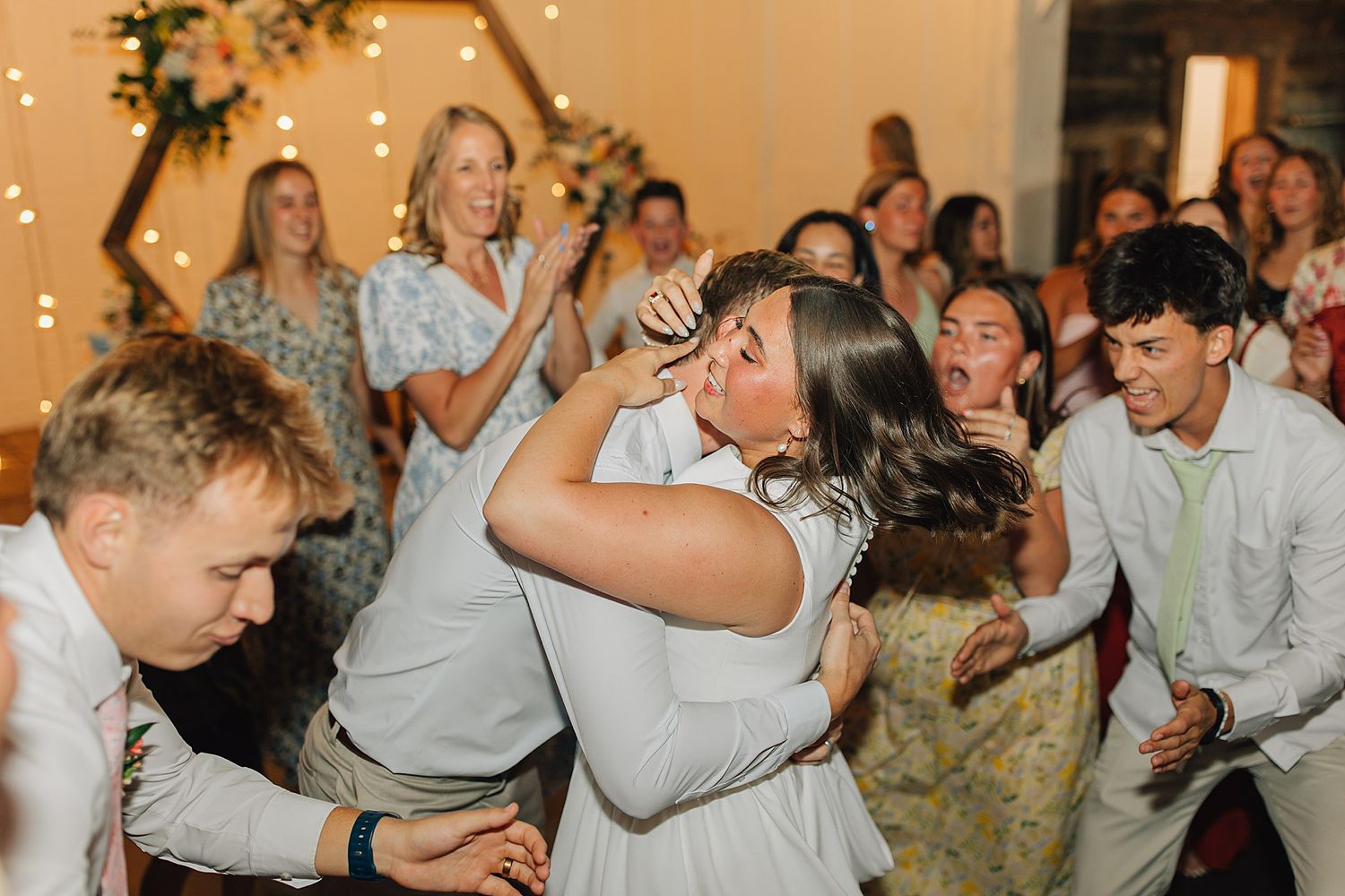 Two wedding guests share a joyful embrace on the dance floor during a lively wedding reception.