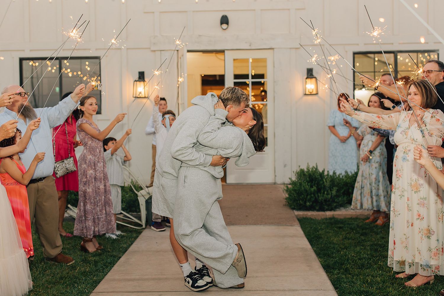 Newlywed couple shares a romantic dip kiss during sparkler send-off at outdoor wedding reception.