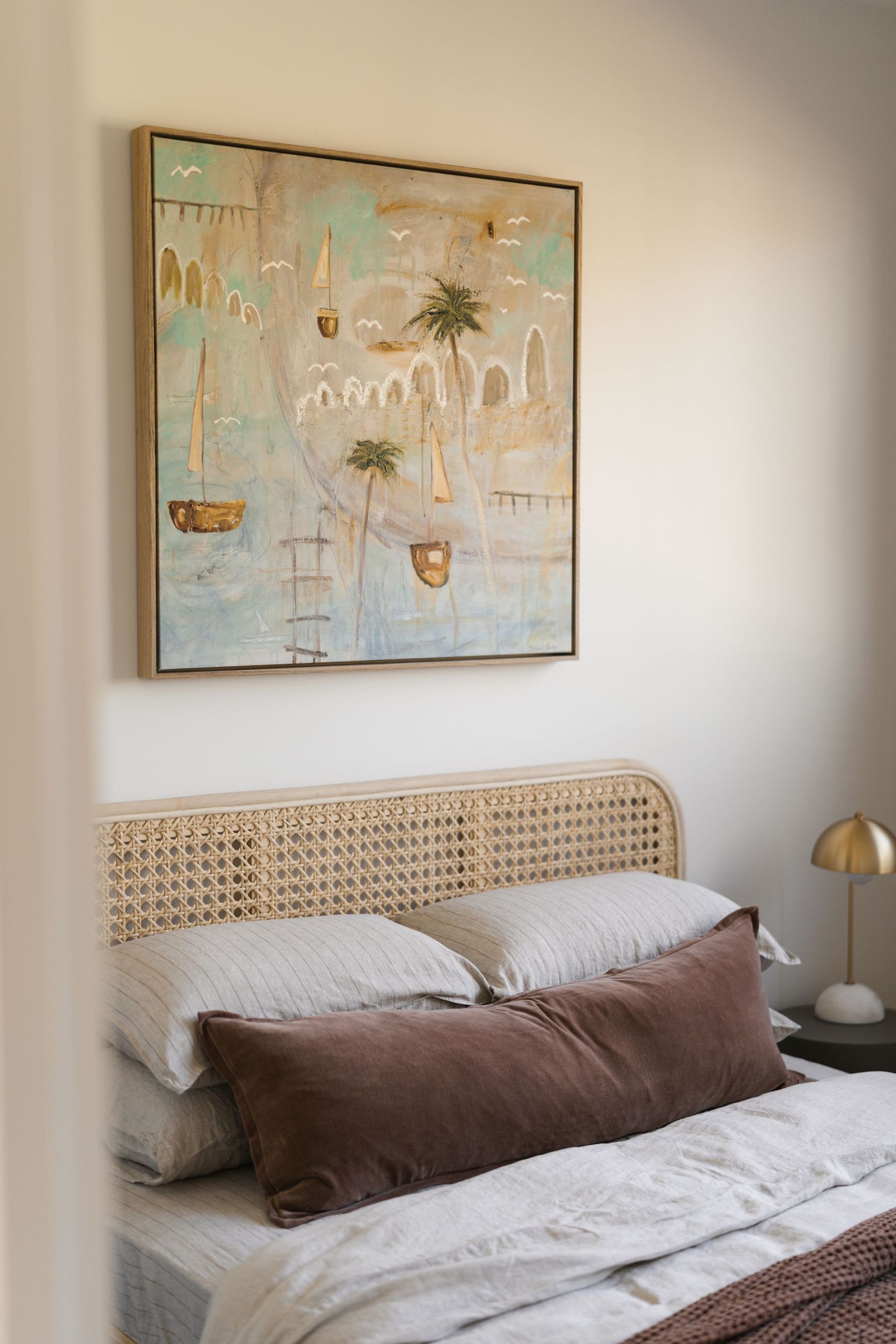 Neutral bedroom with rattan cane headboard, brown velvet pillow, and coastal-themed framed artwork on white wall.

Middleton Fields
