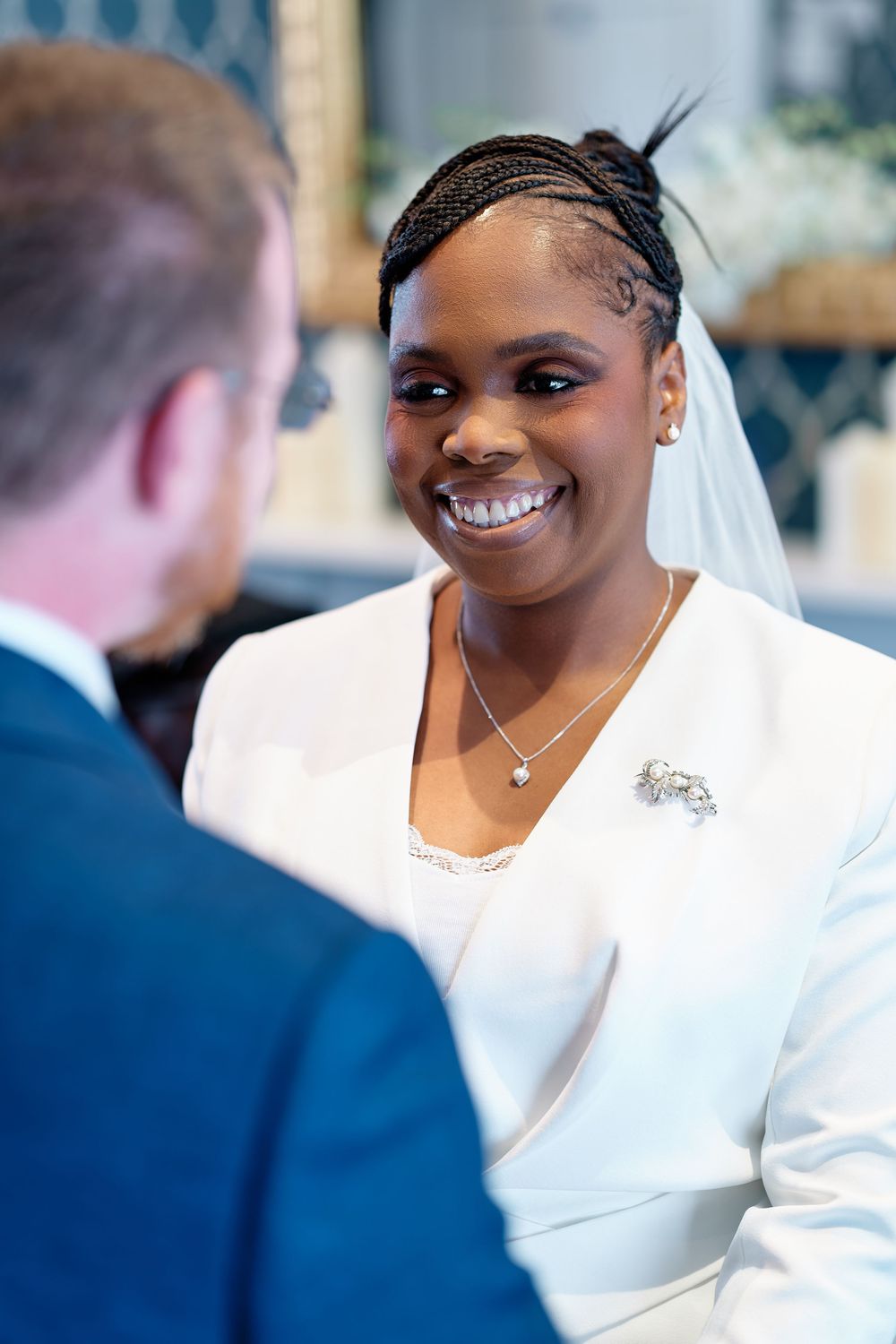 Smiling bride in white dress and veil exchanges vows with groom during wedding ceremony.