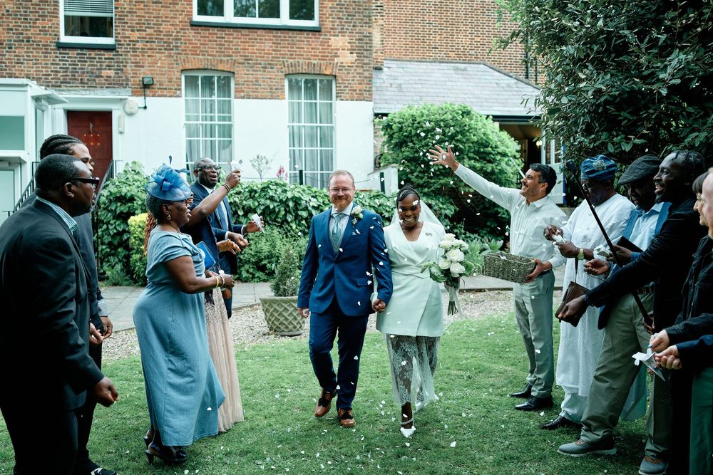 Joyful wedding couple walks through confetti shower surrounded by celebrating guests in a garden ceremony.