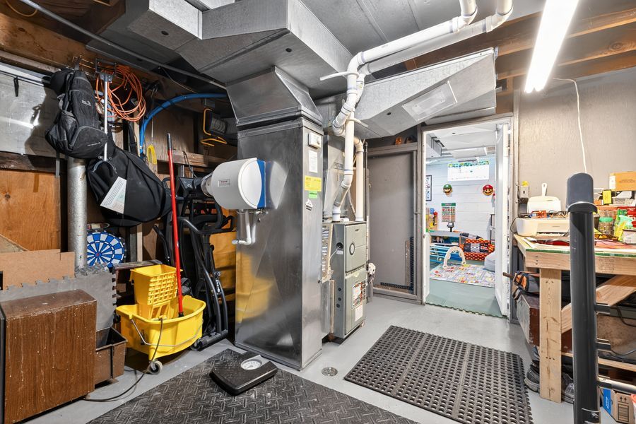 Utility room with furnace, cleaning supplies, yellow mop bucket, and diamond plate flooring leading to a workshop area.