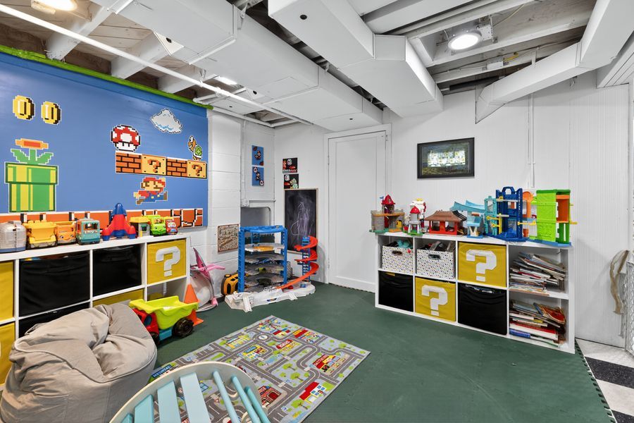 Colorful Super Mario themed kids playroom with toy storage shelves, bean bag chair, and play rug in a finished basement.