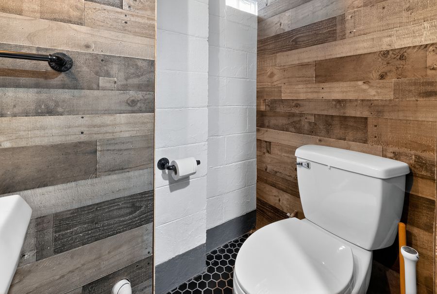 Rustic bathroom with reclaimed wood walls, hexagon tile floors, walk-in shower, and white toilet.