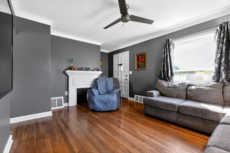 Cozy living room with gray walls, hardwood floors, white fireplace, ceiling fan, and comfortable seating near bright windows.