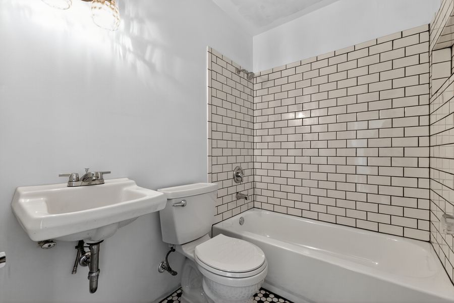 Classic white subway tile bathroom with pedestal sink, toilet, and bathtub with black and white mosaic floor.