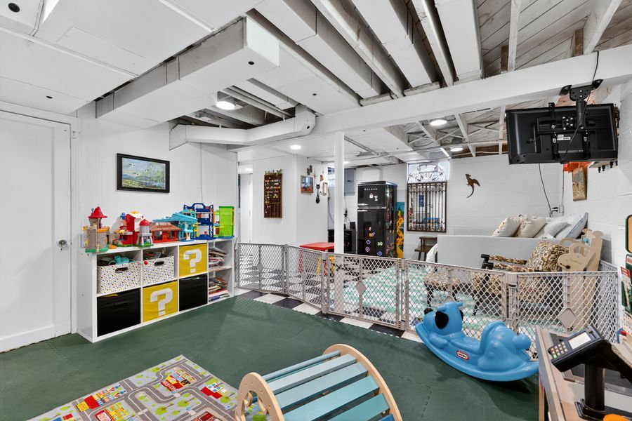 Unfinished basement playroom with colorful toy storage cubbies, checkered floor, and open ceiling beams.