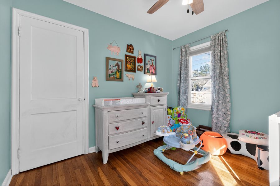 Bright nursery with teal walls, white dresser, hardwood floors, and natural light from a window with gray curtains.