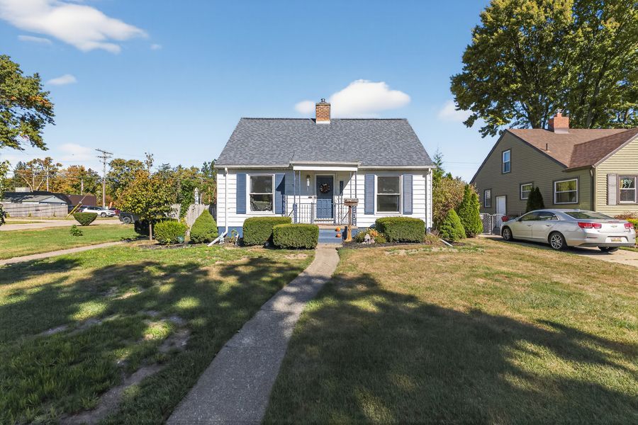Charming Cape Cod home with blue siding, manicured shrubs, lush green lawn, and mature trees in a suburban setting.