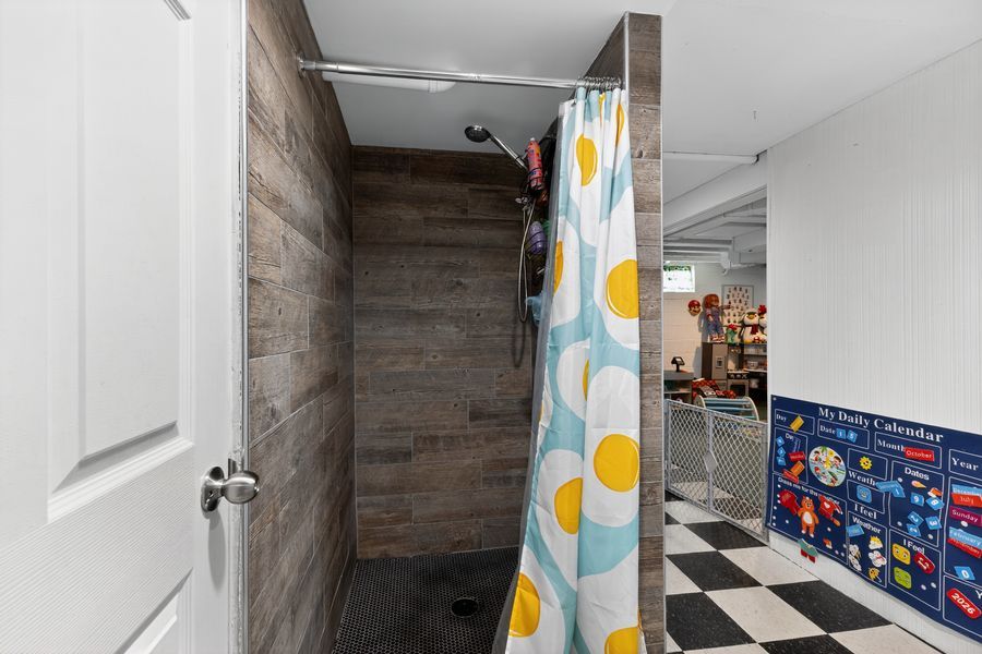 Basement shower with wood-look tile walls, polka dot curtain, and black and white checkered floor.