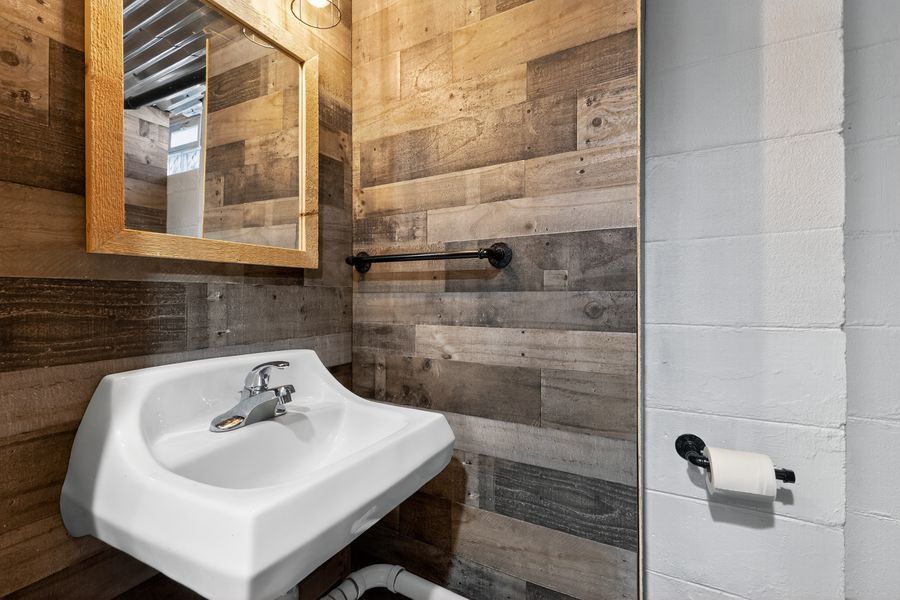 Rustic bathroom with reclaimed wood walls, white wall-mounted sink, framed mirror, and modern fixtures.