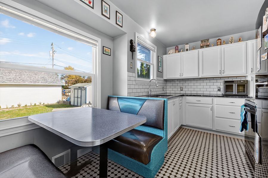 Retro kitchen nook with teal booth seating, chrome table, white cabinets, subway tile backsplash, and checkered floors.
