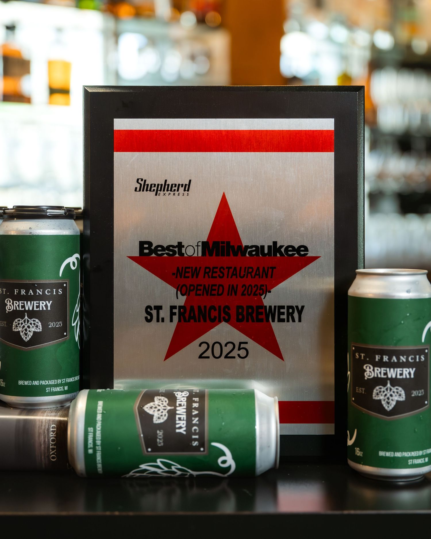 St. Francis Brewery wins Best of Milwaukee 2025 New Restaurant award plaque displayed with green branded beer cans.
