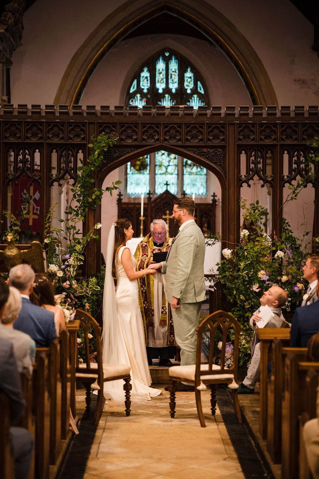 Bride and groom exchange vows at a church altar adorned with floral arrangements and stained glass windows.