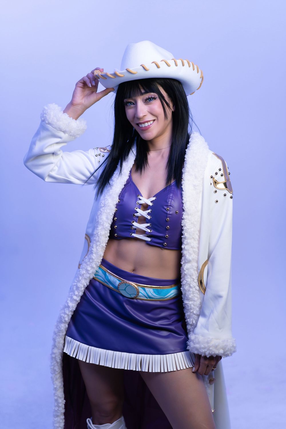 Woman in purple corset top, mini skirt, white fringed coat, and white sombrero posing in cosplay costume.