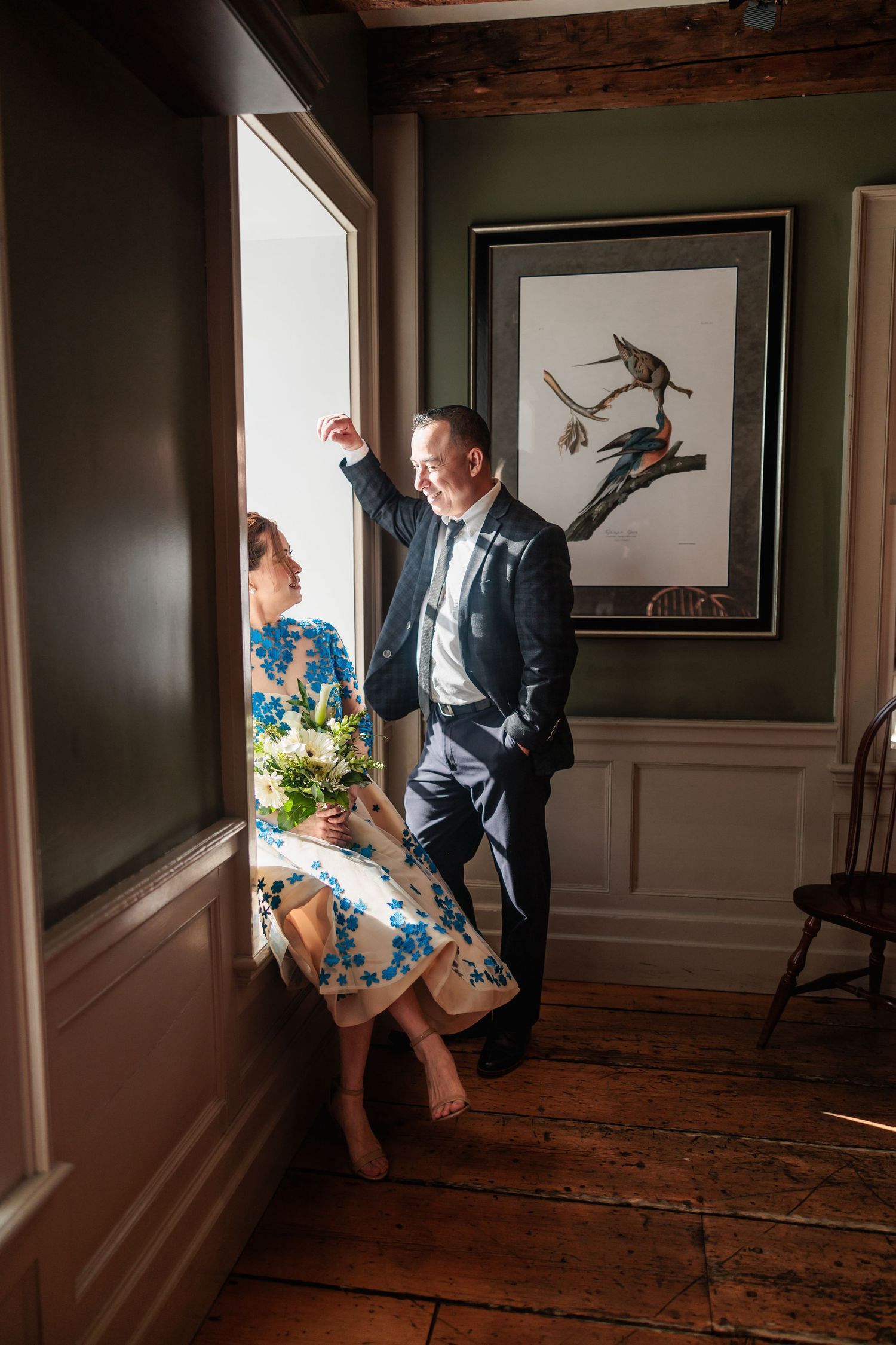 A creative wedding portrait in a rustic indoor setting with dramatic window lighting.