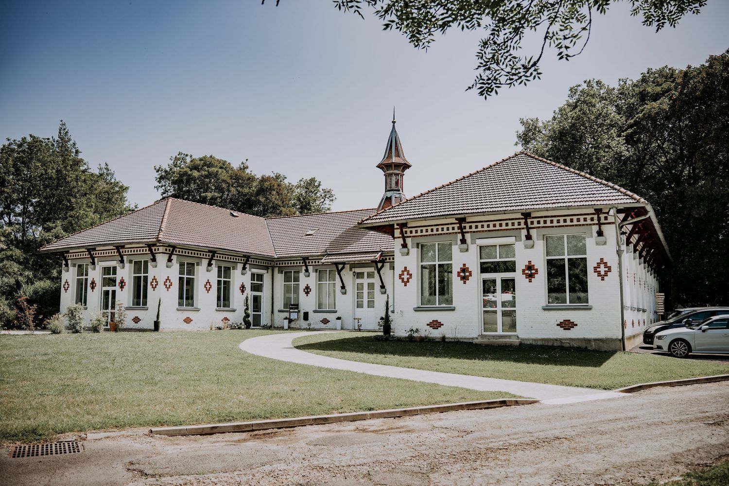 Elegant white Victorian-style building with ornate trim, small spire, and manicured lawn surrounded by lush trees.