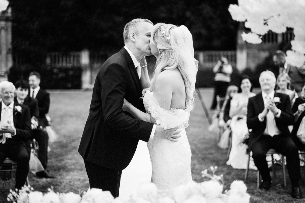 Black and white photo of a bride and groom sharing their first kiss at an outdoor wedding ceremony.