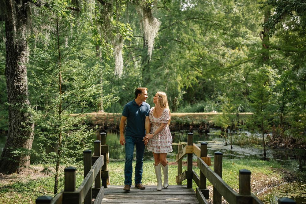 Couple holding hands on a wooden bridge in a lush green forest setting.