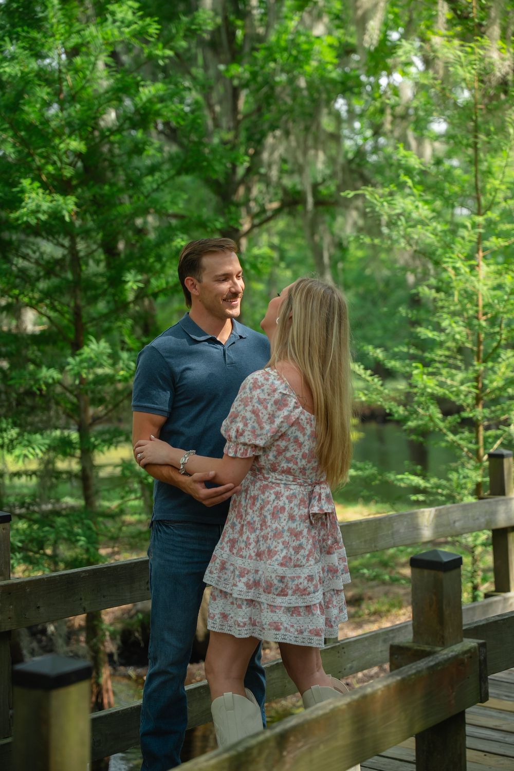 Smiling couple holding hands on a wooden deck surrounded by green trees.