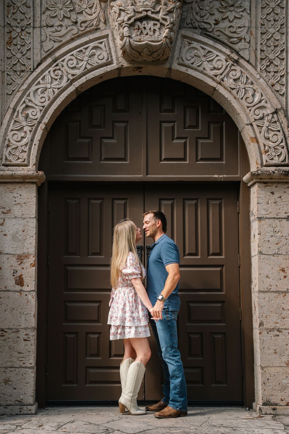 Couple holding hands in front of an ornate arched wooden door.