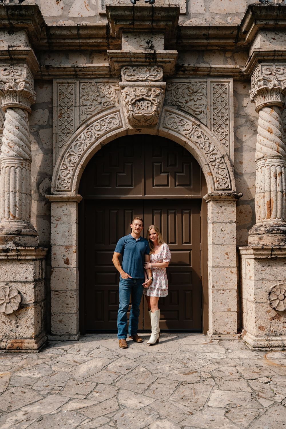 Couple posing together in front of an ornate carved stone archway entrance.