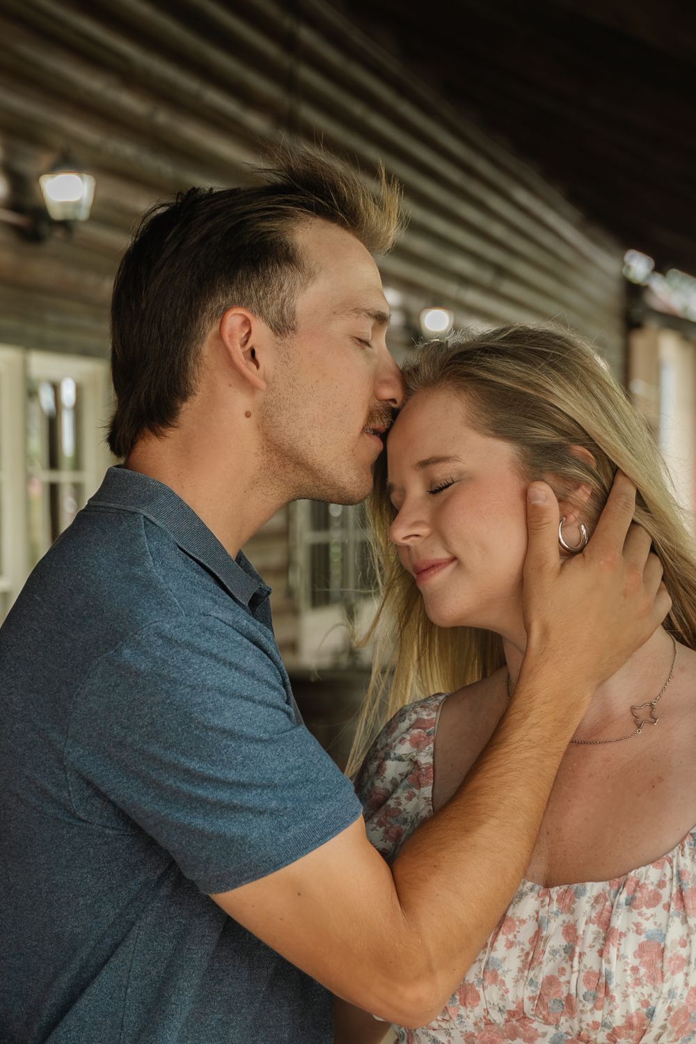 Man tenderly kissing womans forehead while cradling her face during a romantic outdoor couples session.