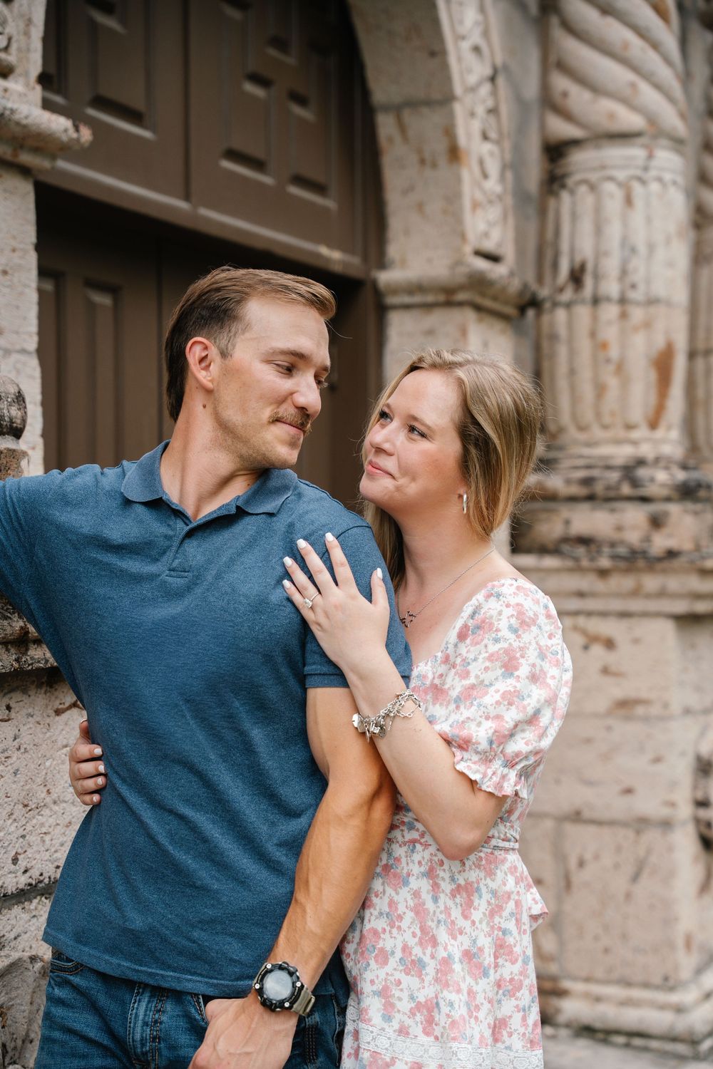 Couple sharing a tender moment against an ornate stone building facade.