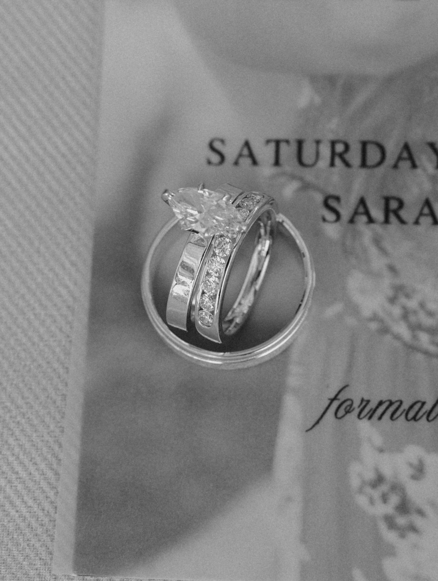 Close-up of wedding rings resting on a printed invitation suite, captured as timeless wedding detail photography.