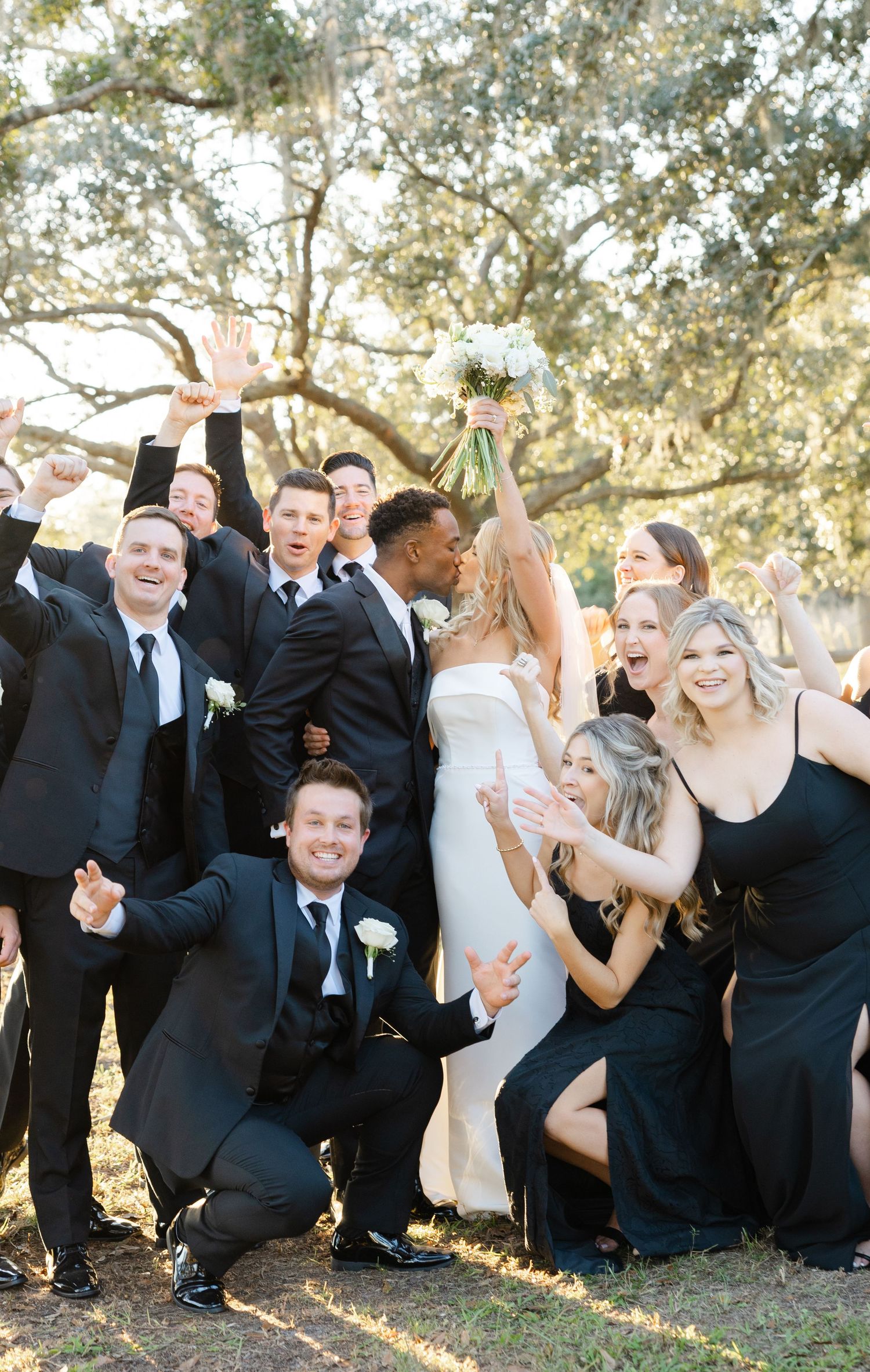 Wedding party gathered together outdoors beneath trees during a wedding day portrait session.