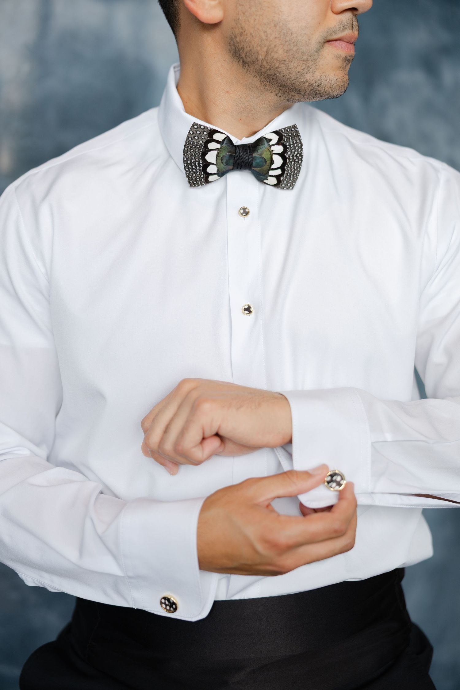 Groom adjusting cufflinks while wearing a white dress shirt and bow tie, photographed during wedding day preparations.