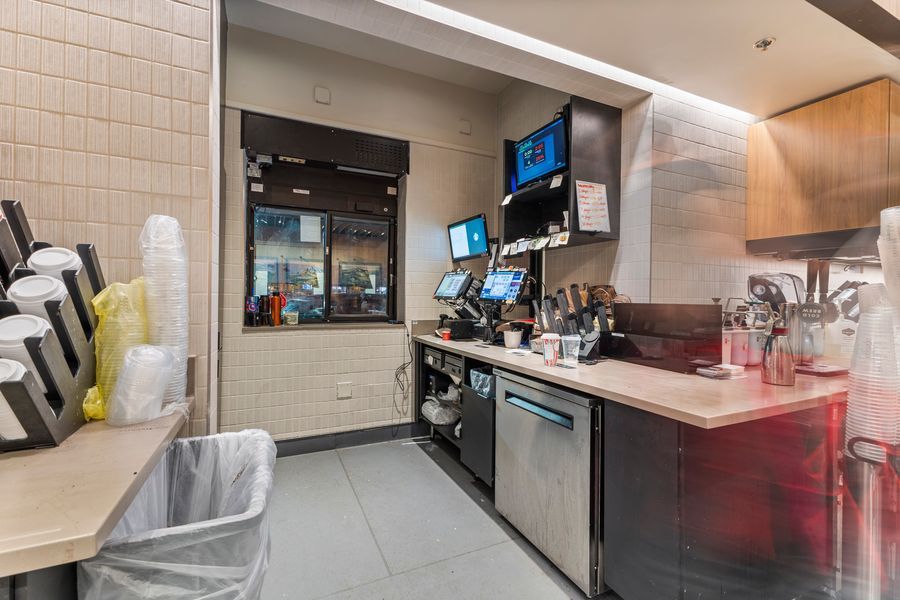 Modern fast food restaurant back-of-house prep area with stainless steel equipment, POS screens, and organized counter workspace.