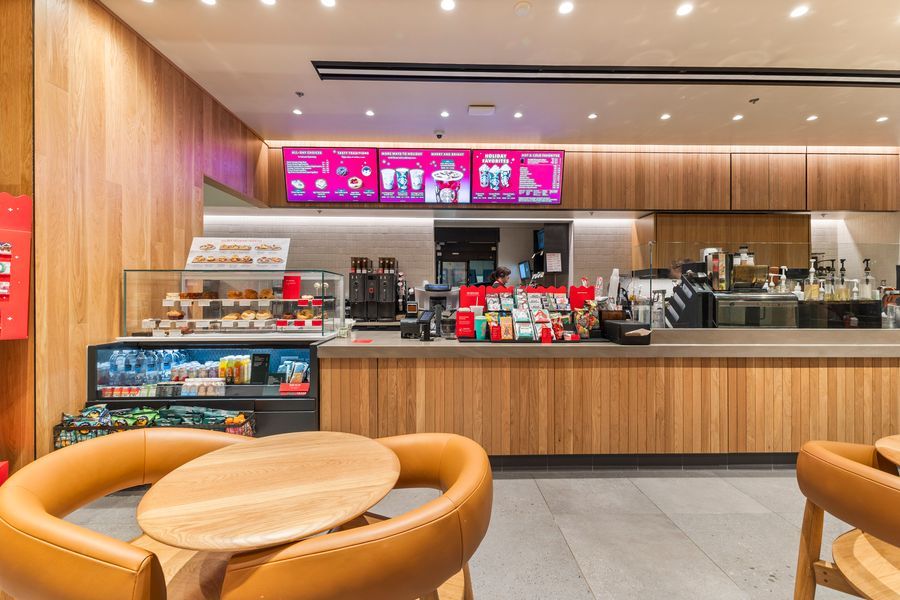 Modern Dunkin' coffee shop interior with wooden counter, digital menu boards, and cozy leather seating area.