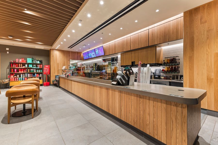Sleek modern cafe counter with warm wood paneling, menu display screens, and retail shelving in a contemporary setting.