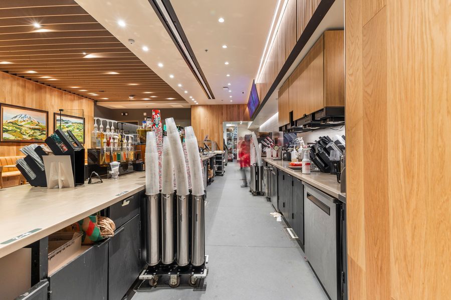 Commercial cafe kitchen prep area with stainless steel counters, cup dispensers, and wood ceiling accents.