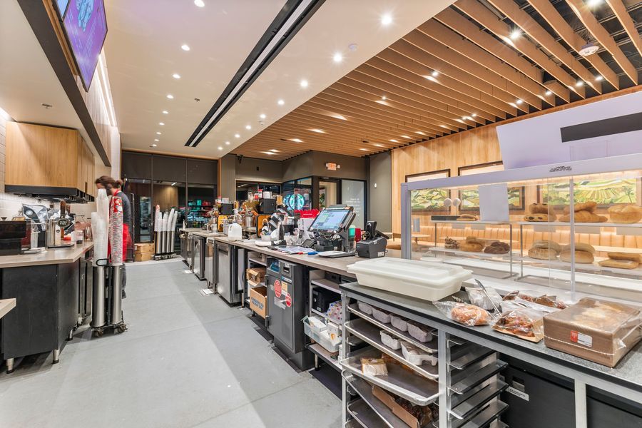 Bright modern commercial kitchen with wood slat ceiling, stainless prep stations, and large windows overlooking outdoor area.