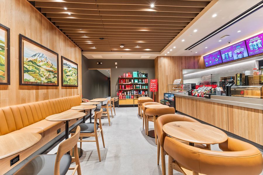 Modern fast food restaurant interior with wooden booths, round tables, and a colorful menu display board.