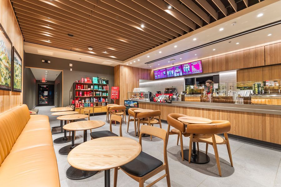 Modern Starbucks cafe interior with wood paneling, round tables, cushioned booths, and a bright service counter.