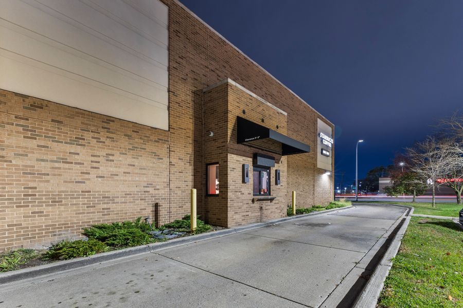 Nighttime exterior of a brick commercial building with illuminated entrance, parking lot, and green landscaping under a dark sky.
