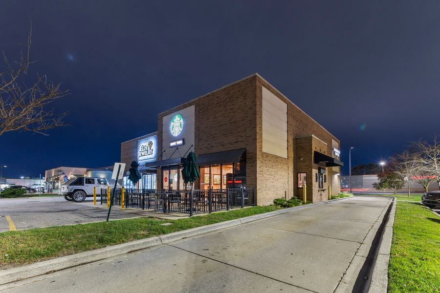 Starbucks restaurant exterior at night with brick facade, outdoor seating, and illuminated signage.