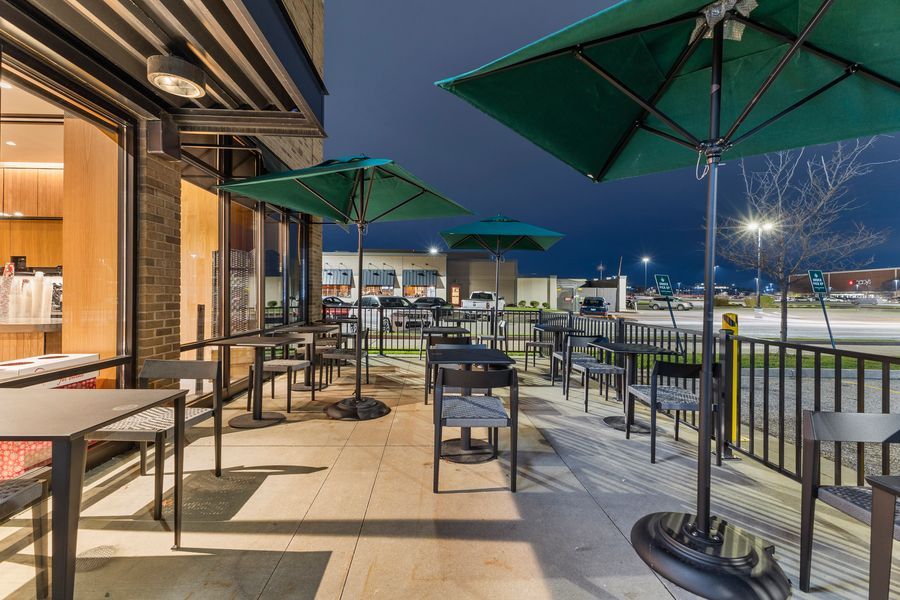 Starbucks outdoor seating area at night with green patio umbrellas and chairs along a well-lit storefront.