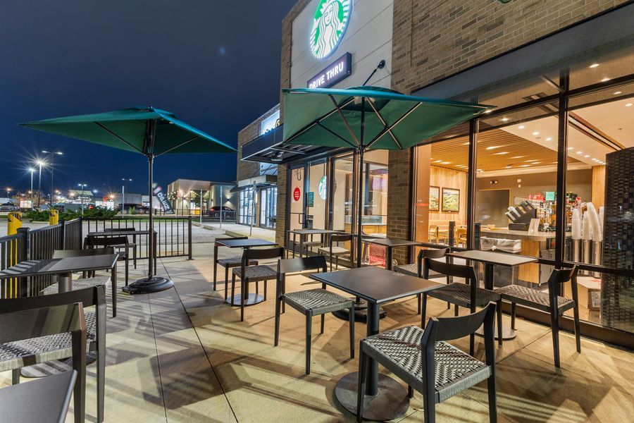 Starbucks outdoor patio at night featuring green umbrellas and dark metal chairs with parking lot view.