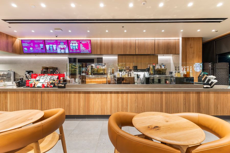 Modern Starbucks cafe interior with warm wood counter, digital menu boards, and round leather seating.