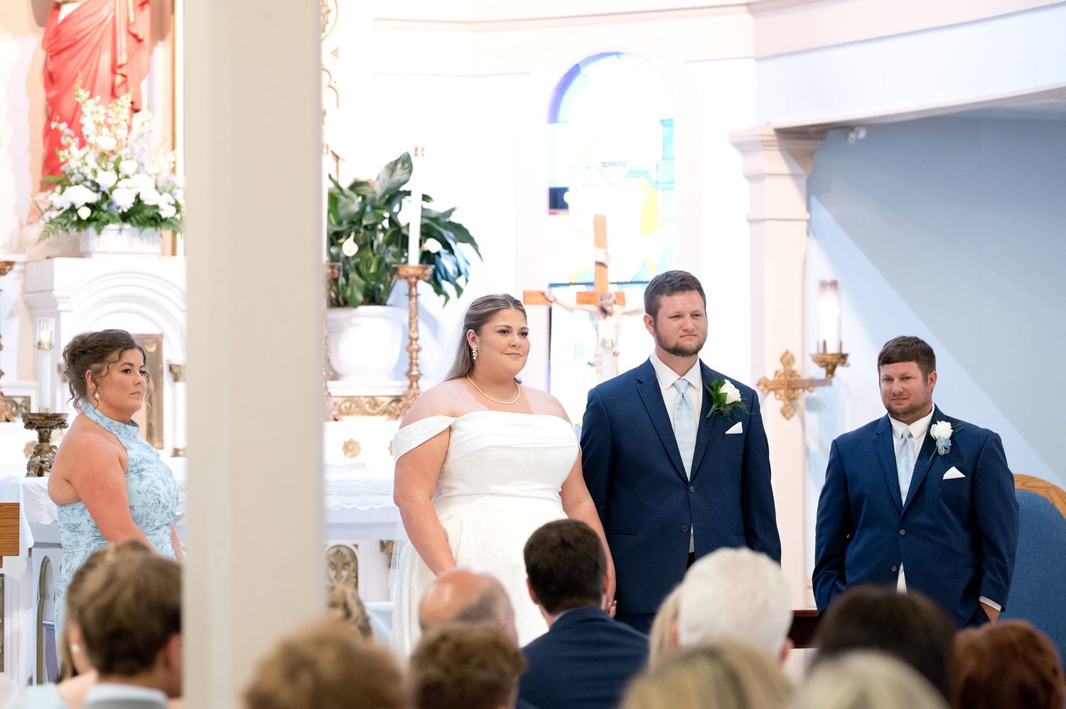 Bride and groom stand at the altar during a church wedding ceremony with wedding party members beside them.