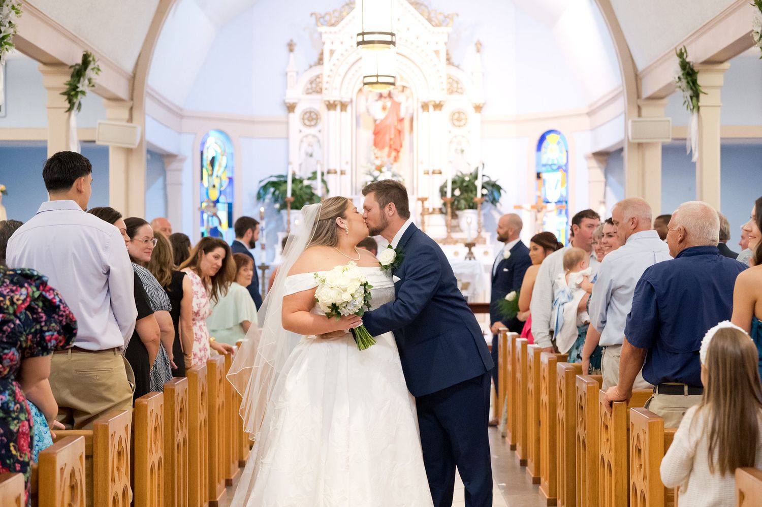 Bride and groom share first kiss as newlyweds in a charming blue and white church.